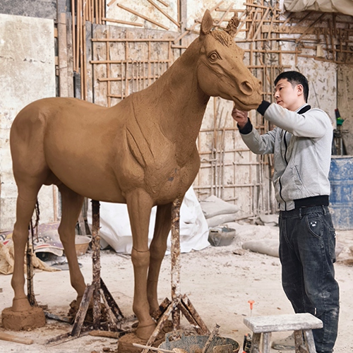 An artist is creating a clay model of a standing horse sculpture.