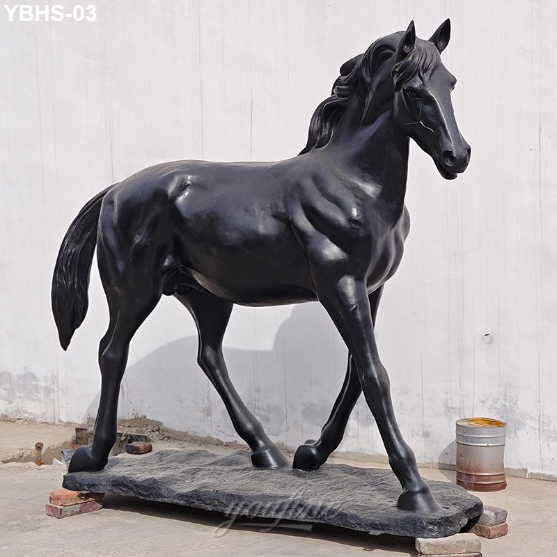 A sleek black bronze horse statue with fine detailing, standing on a stone base in an outdoor environment against a white wall.