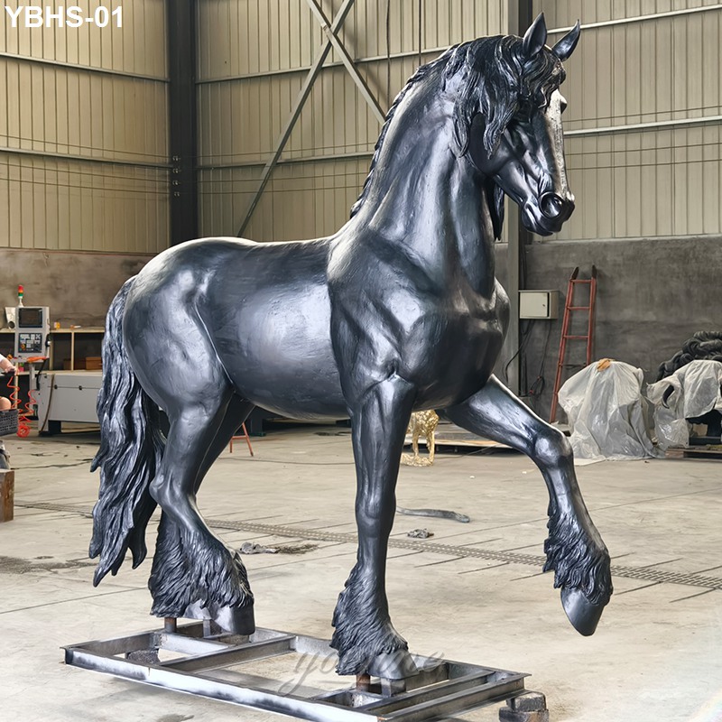A large bronze Friesian horse sculpture with intricate detailing on mane and hooves, displayed inside a professional workshop.