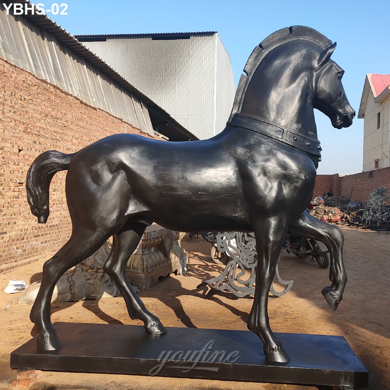 A sleek bronze horse sculpture with detailed musculature and a raised front leg, displayed outdoors
