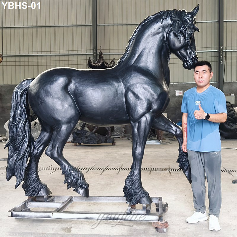 A large black bronze Friesian horse sculpture on a metal base in a workshop setting,