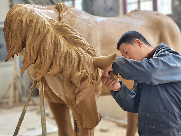 Master sculptor hand-building clay model of rearing bronze horse