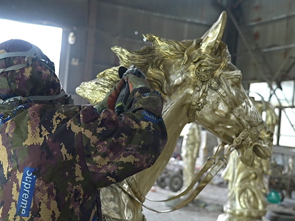 Hand chasing surface detail on bronze horse sculpture -- muscle lines and mane texture