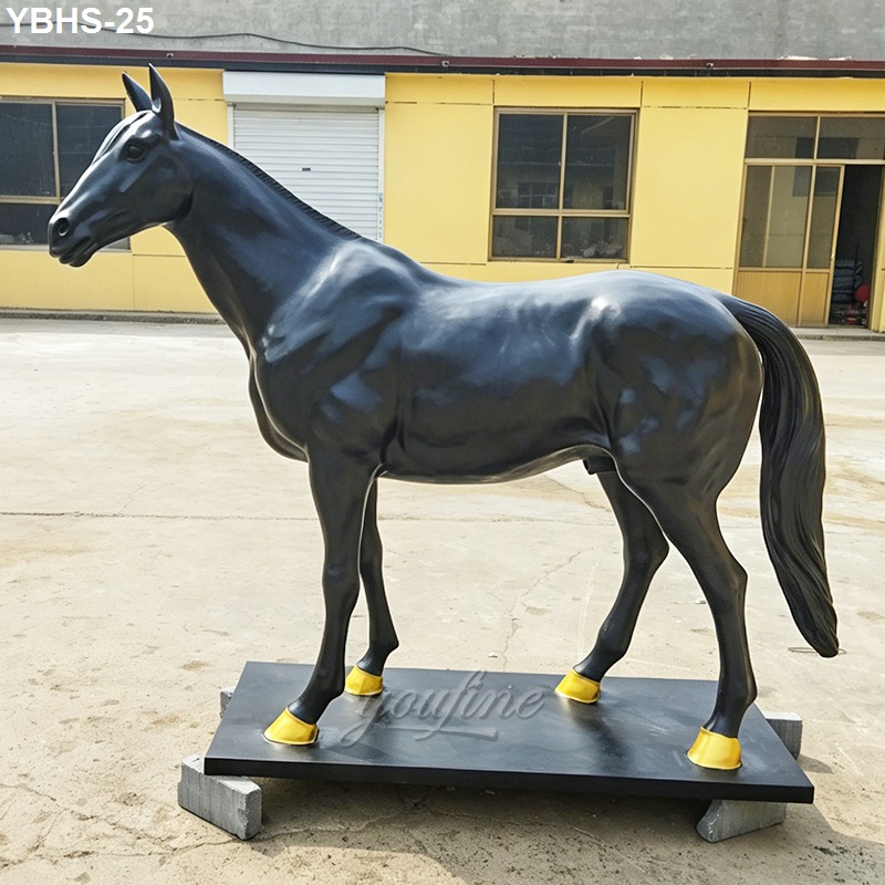 Black bronze horse sculpture with gold accents on hooves standing on a sturdy platform outdoors in front of a yellow building.