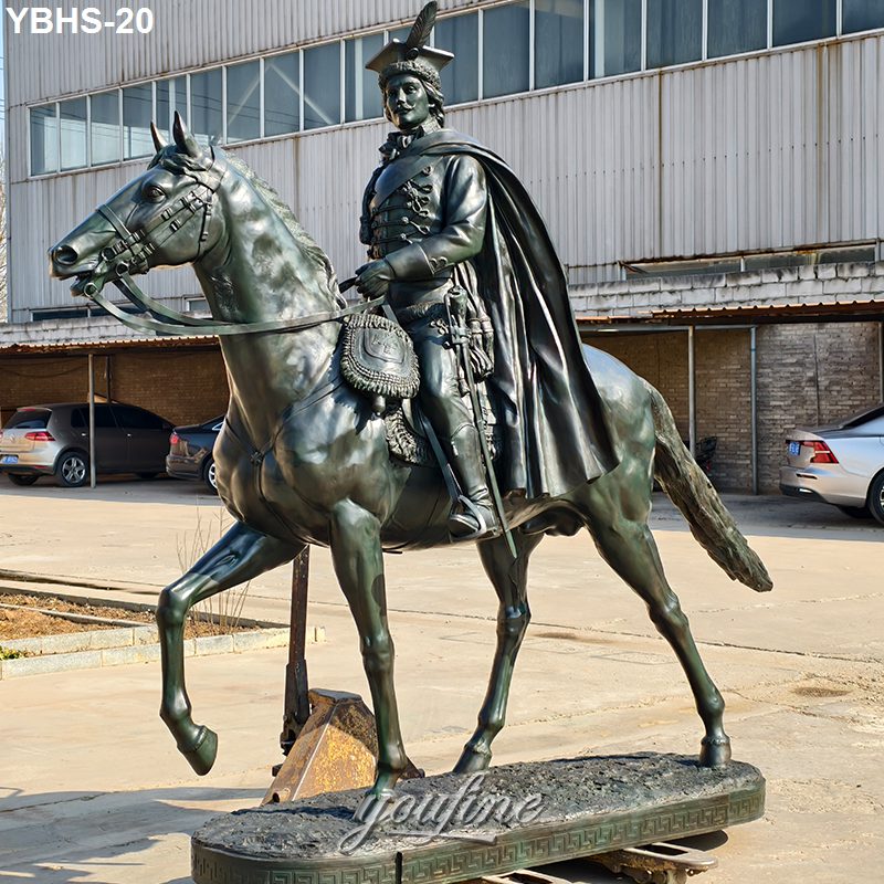 Bronze equestrian statue depicting a detailed rider in uniform on a horse, located outdoors near industrial buildings.