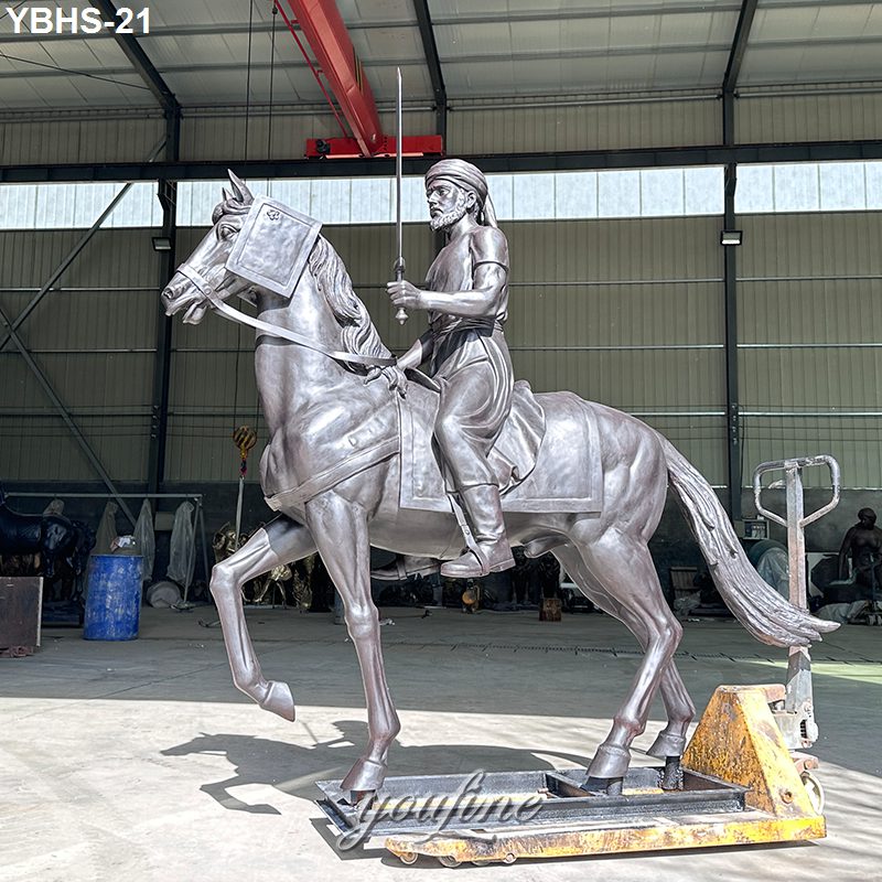 Bronze statue of a rider on horseback holding a sword, displayed indoors on a moving platform with industrial surroundings.
