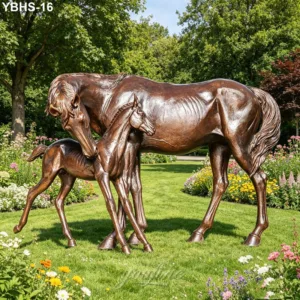 Elegant bronze horse and foal sculpture surrounded by colorful flowers and greenery in a landscaped garden during daylight.