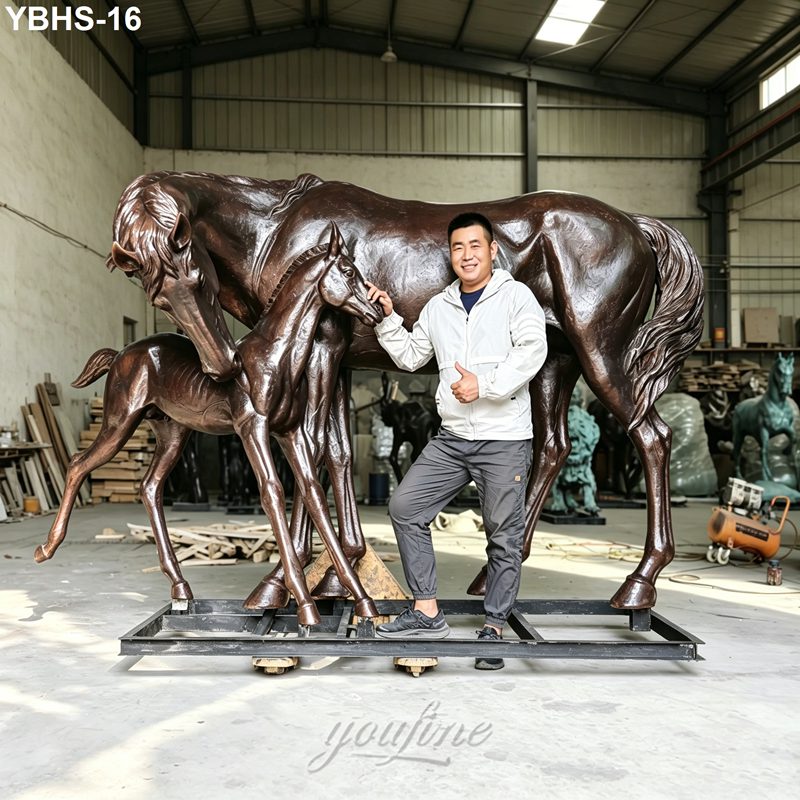 A bronze sculpture of a horse and foal displayed in a workshop setting, with a person standing beside for scale.