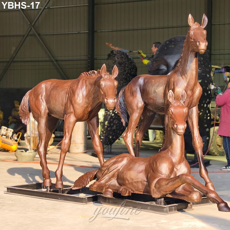 Bronze sculpture of horse family featuring adult and foal horses in varying poses, displayed in a workshop setting.