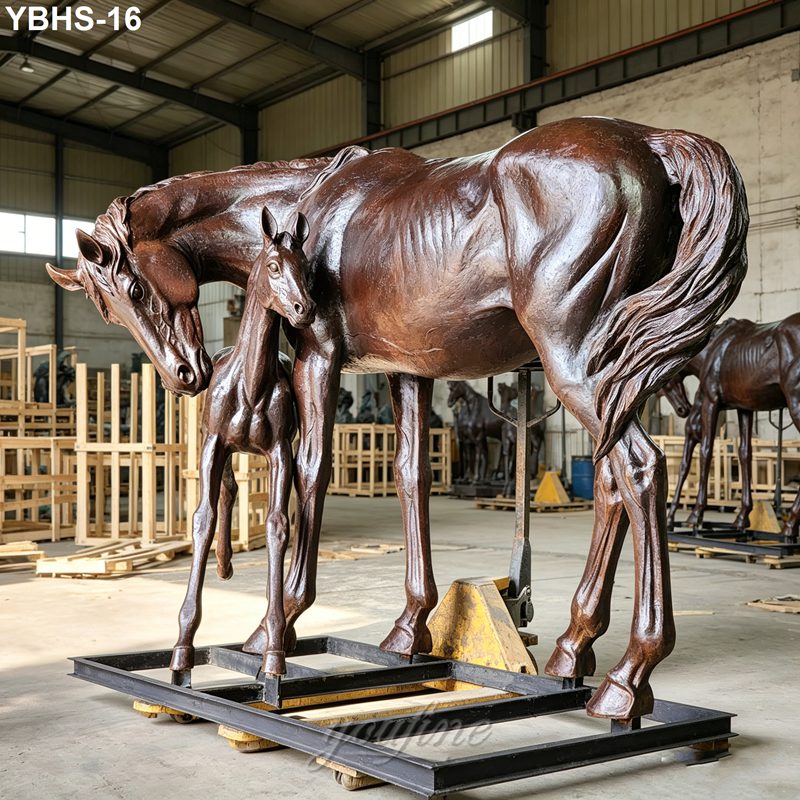 Large bronze horse sculpture depicting a mare and foal in an artisan workshop, with wooden crates and tools in the background.