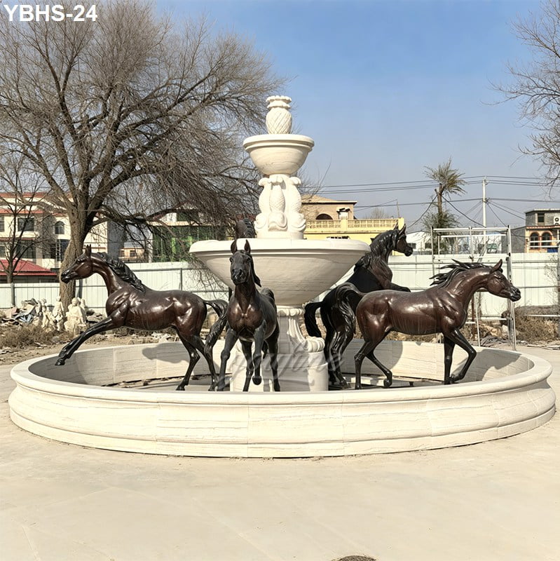 A circular fountain featuring detailed bronze horse sculptures surrounding a central white-tiered structure, set outdoors.