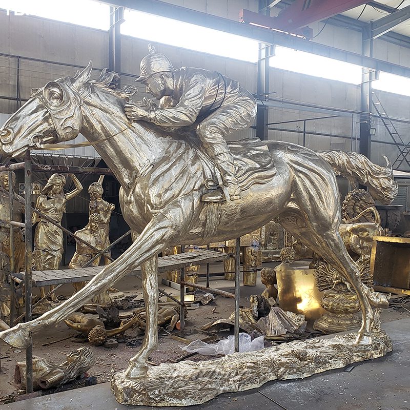 Bronze sculpture of a horse and jockey in dynamic motion being crafted in a workshop setting with other sculptures visible.
