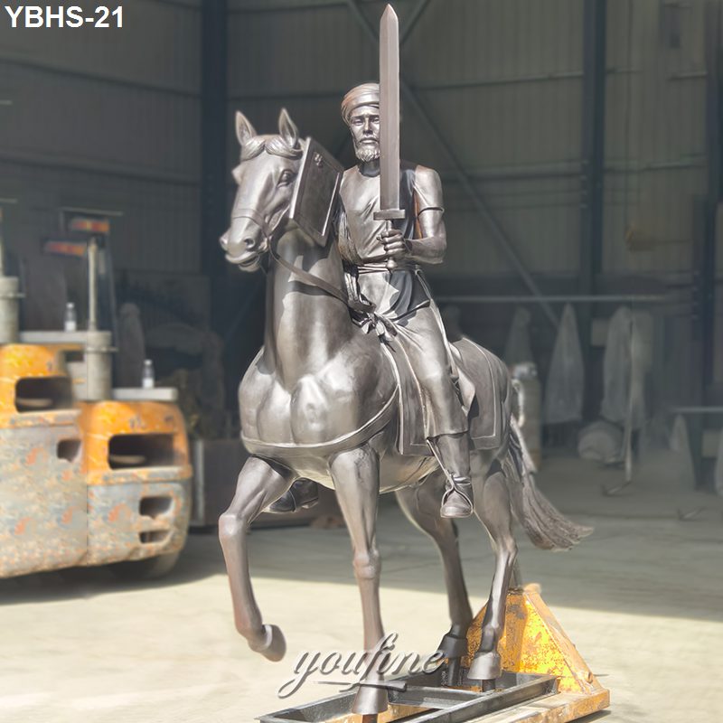 Bronze sculpture of a knight on a galloping horse holding a sword, crafted in detailed armor in an industrial setting.