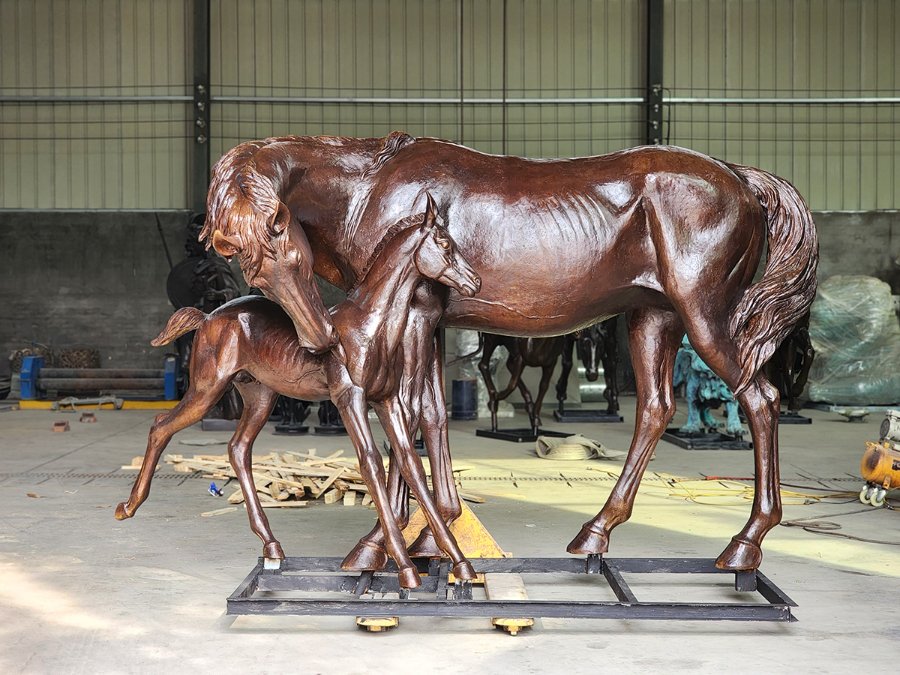 Elegant bronze sculpture of a mare and foal, showcasing lifelike details and craftsmanship, placed in an industrial workshop setting.