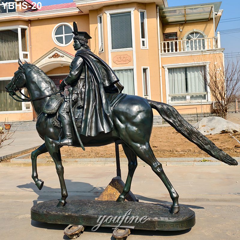 A detailed bronze sculpture of a rider in historical attire on horseback, placed outdoors near a large building with landscaped surroundings.