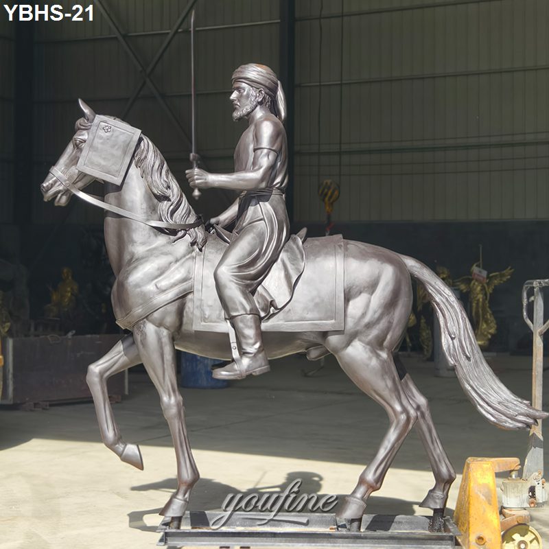 A detailed bronze statue of a rider on horseback holding a sword, displayed in an industrial workshop setting.