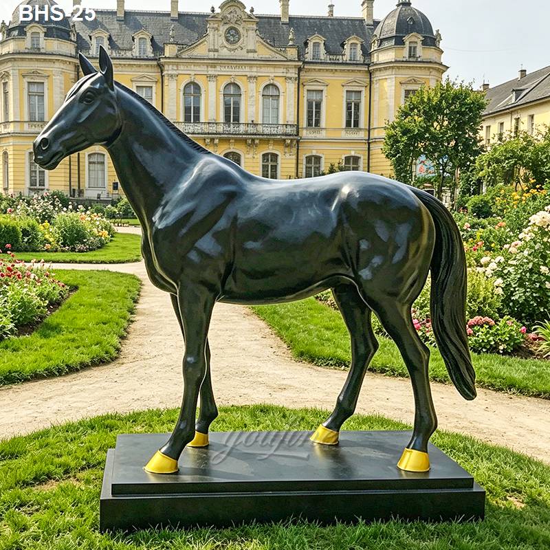 Elegant bronze horse sculpture with gold accents on hooves displayed in a manicured garden outside a grand castle.