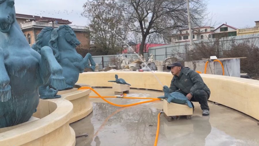 The bronze horse sculpture fountain is undergoing water testing, and a worker is adjusting the water flow.
