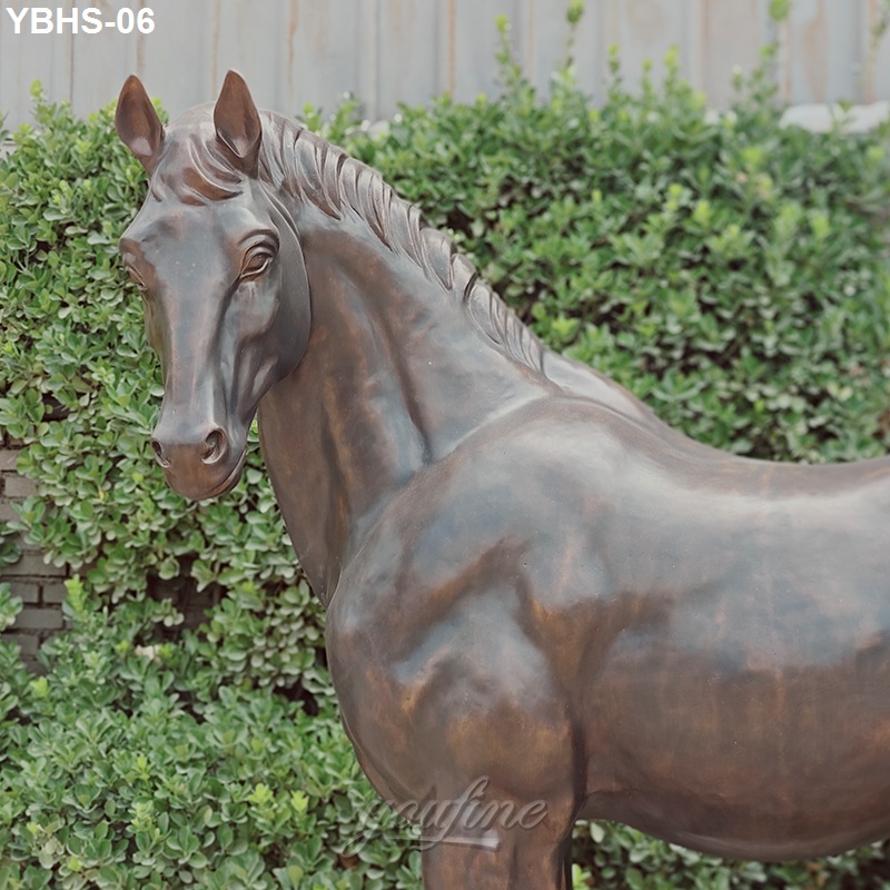 Realistic bronze horse sculpture with intricate detailing displayed outdoors with greenery and wooden fencing in the background.