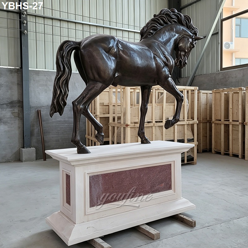 Bronze horse sculpture with detailed mane and muscular stance atop a decorative pedestal in an indoor workshop setting.