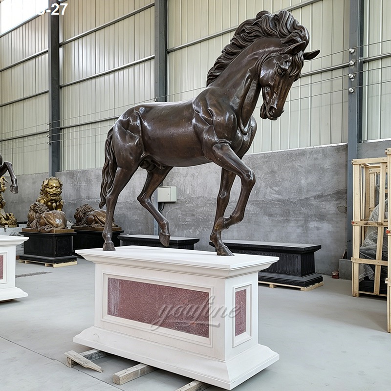 Detailed bronze horse sculpture with flowing mane displayed on a white and red-stone pedestal in an industrial workshop.