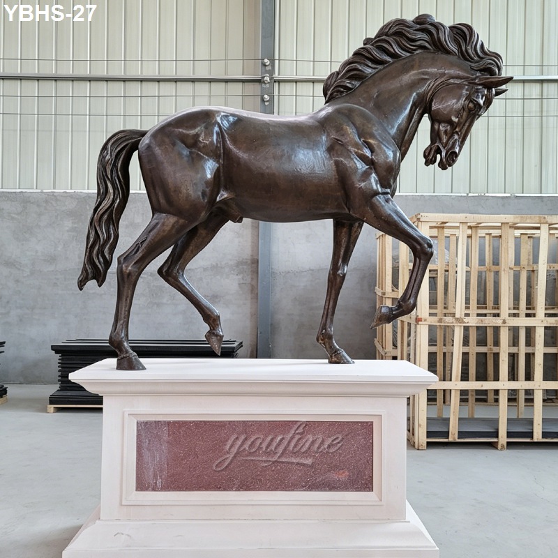 Bronze standing horse sculpture with flowing mane posed on a white decorative pedestal inside a modern workshop.