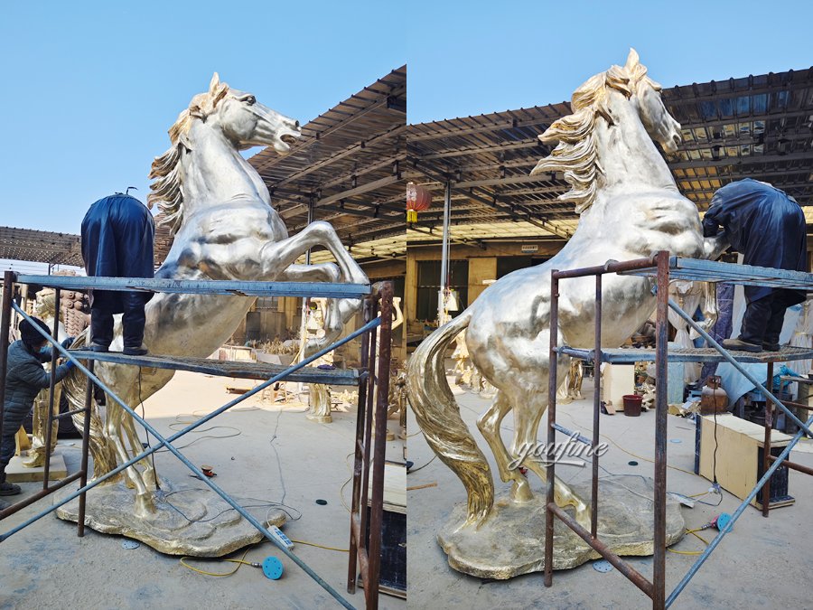 Large rearing bronze horse sculpture being polished by workers in an industrial workshop. The statue features intricate mane and tail details.