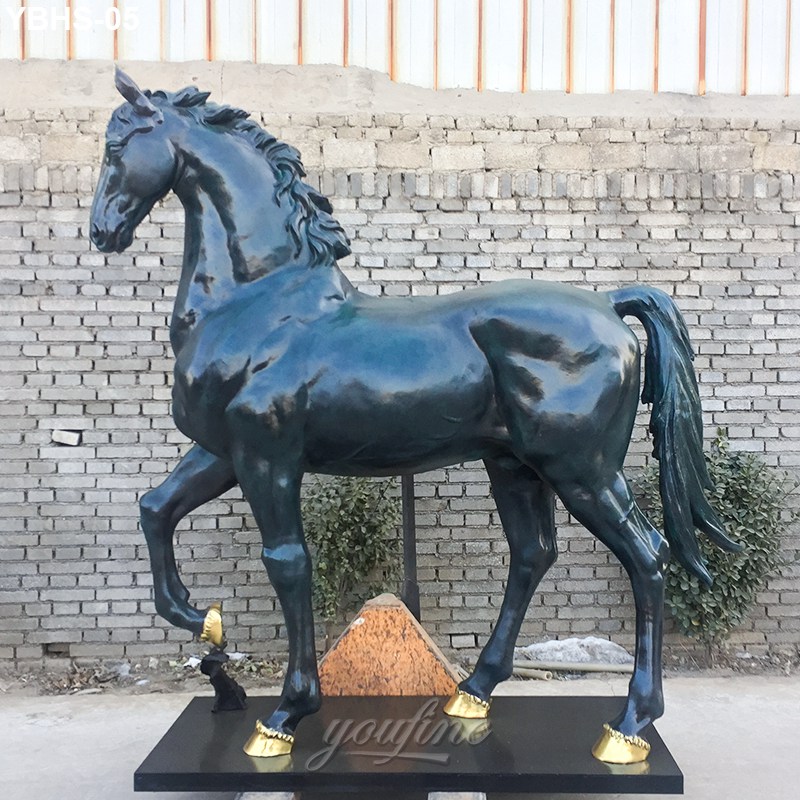 Large bronze horse sculpture with golden hooves, standing on a black base against a brick wall backdrop.