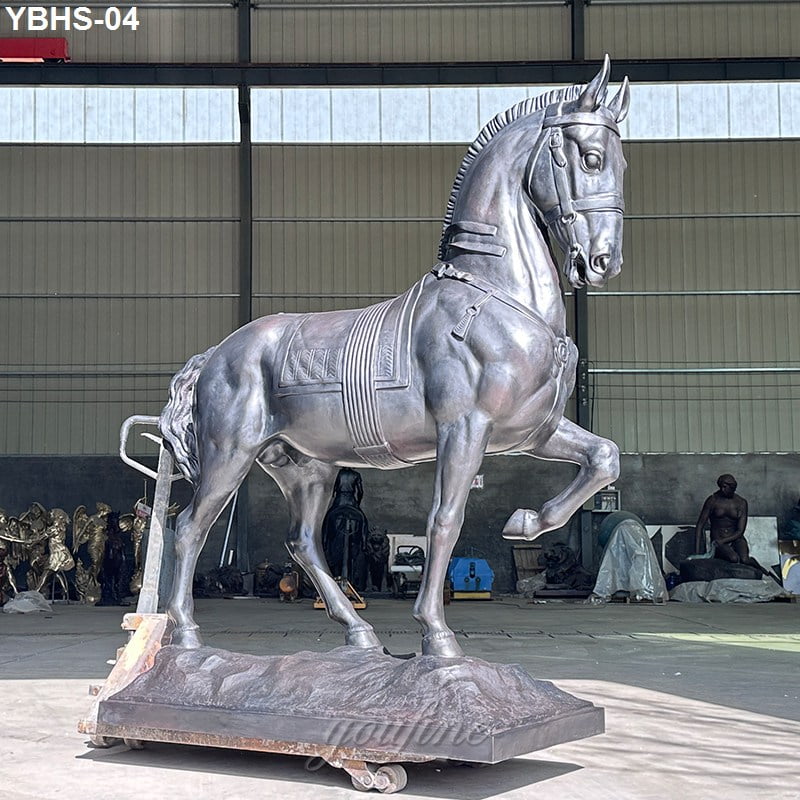 A life size bronze horse sculpture standing proudly on a decorative base inside a studio, surrounded by various artworks and equipment.