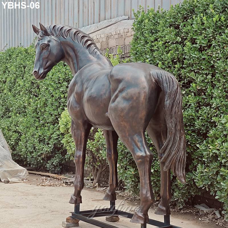 A detailed bronze horse sculpture with lifelike features placed in an outdoor setting, surrounded by greenery and industrial elements.