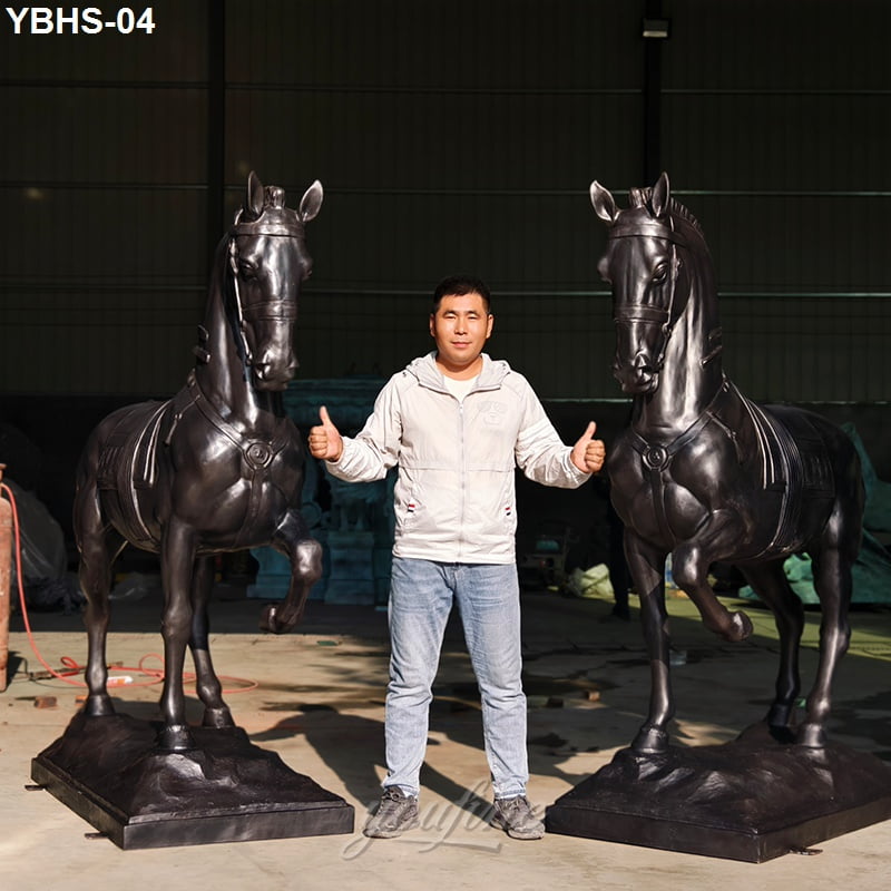 Person giving thumbs up between two large bronze horse sculptures in an indoor space.