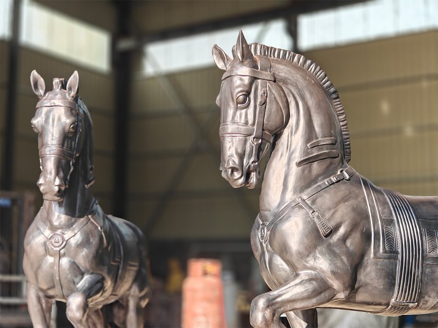 Two intricately detailed bronze horse sculptures displayed in a workshop setting, showcasing craftsmanship and metallic sheen.