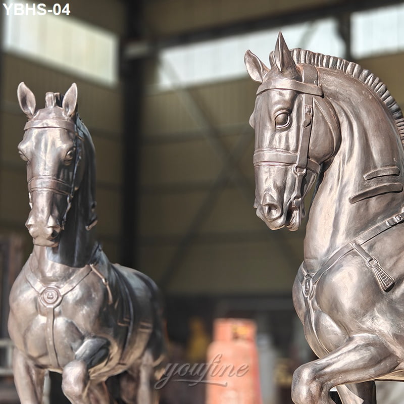 Two exquisitely crafted bronze horse sculptures featuring lifelike details and harnesses, displayed in an industrial workshop.
