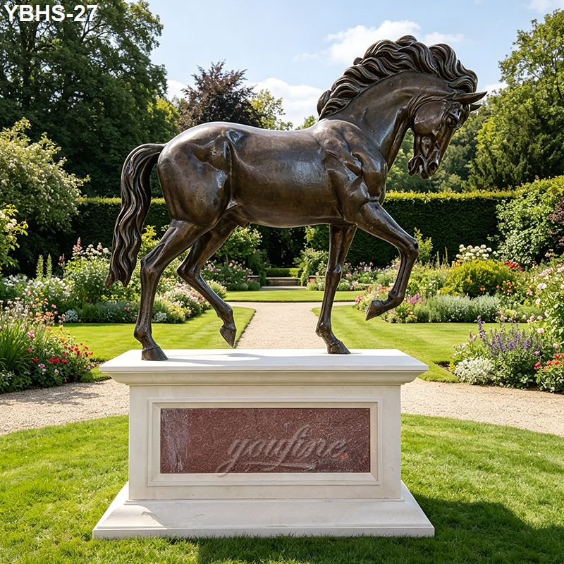 A majestic standing bronze horse statue with flowing mane on a stone pedestal, set in a landscaped garden with flowering plants and hedges.