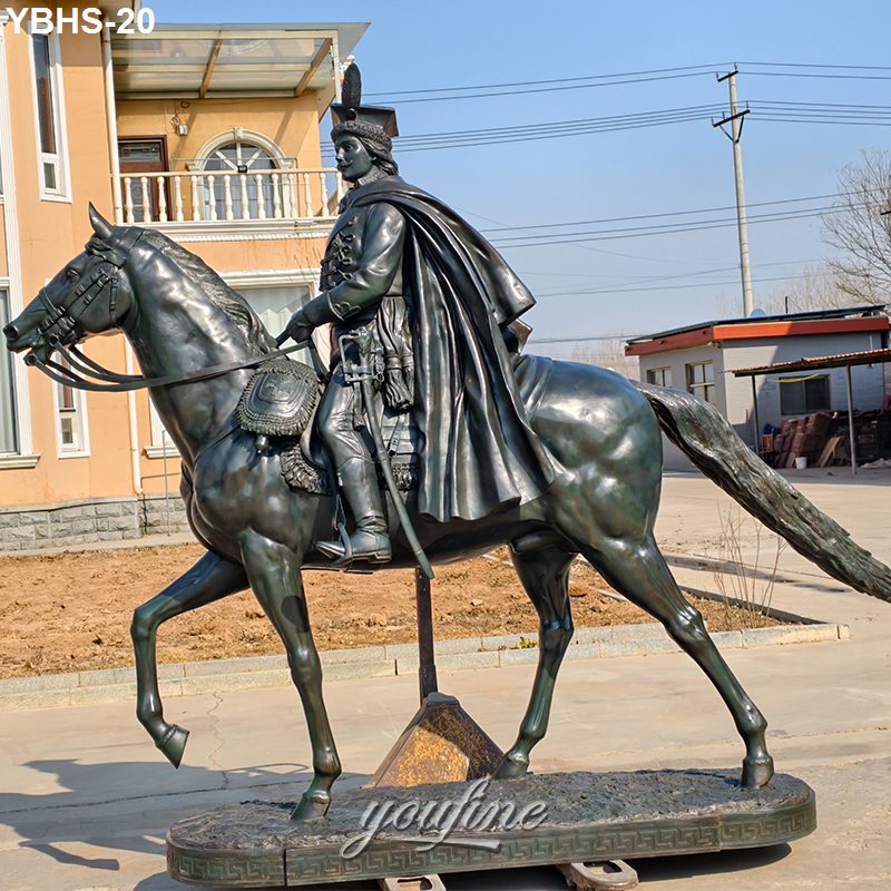Bronze horse statue featuring a rider in historical attire with cape and hat, posed outdoors near buildings under clear blue sky.