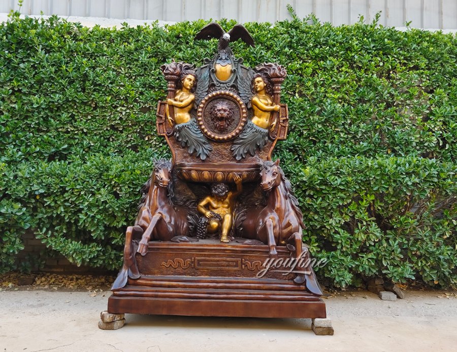 Ornate bronze wall fountain featuring detailed horse figures, lion emblem, and golden accents set against lush greenery outdoors.