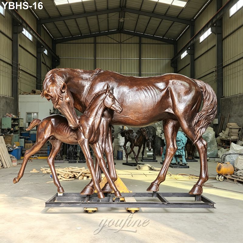 A detailed bronze sculpture of a mare and foal displayed in an industrial workshop, showcasing artistic craftsmanship and equestrian themes.
