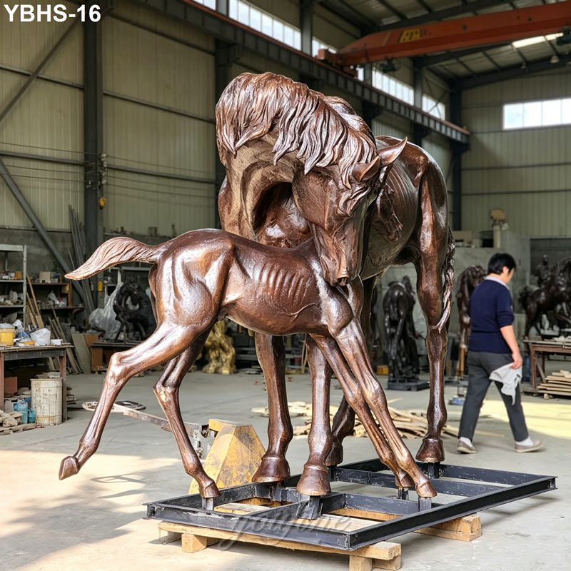 A detailed bronze sculpture of a mare with her foal, displayed in a workshop setting, showcasing intricate craftsmanship.