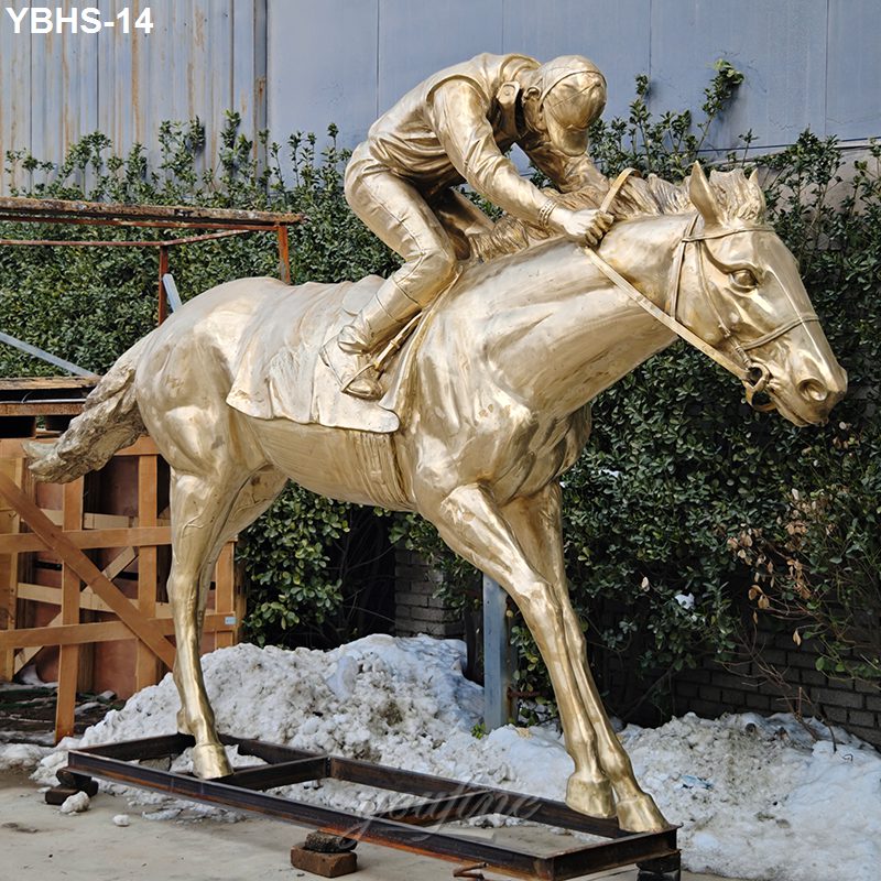 Golden bronze sculpture of a racehorse with a jockey in a dynamic racing pose, displayed outdoors near bushes and a warehouse.