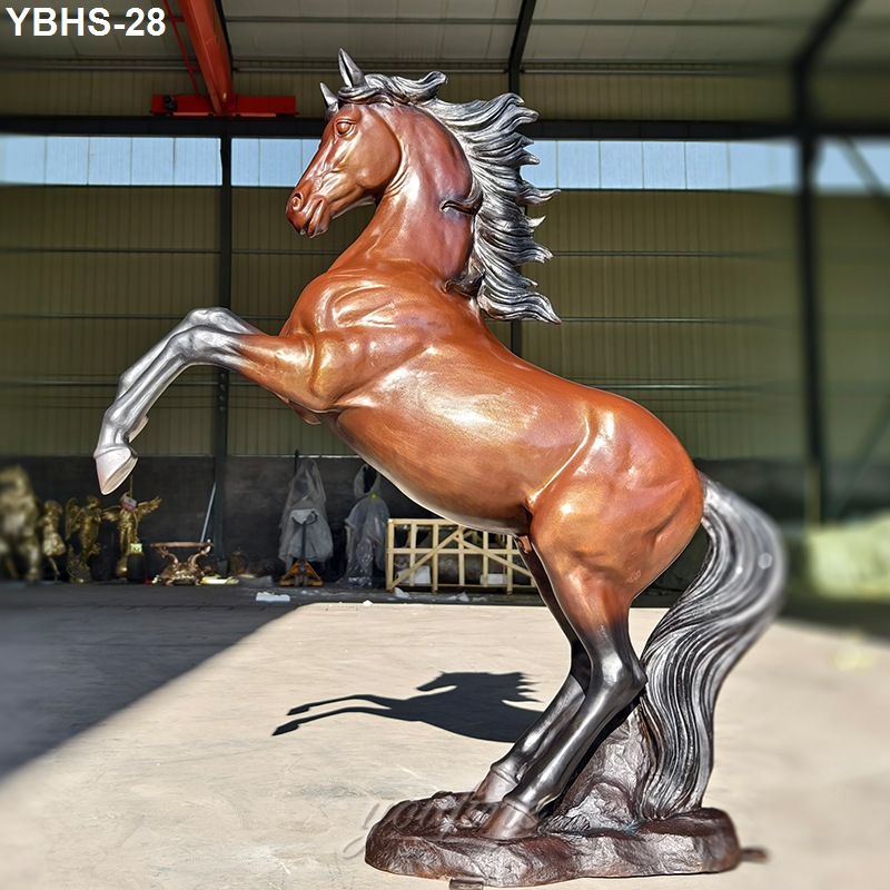A polished bronze sculpture of a rearing horse with intricate mane and tail detailing, displayed in a workshop setting.