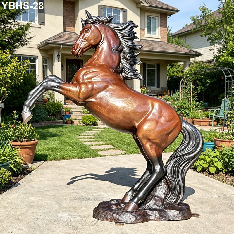 Bronze horse sculpture depicting a rearing pose with detailed mane and tail, placed on a garden pathway near a residential property.