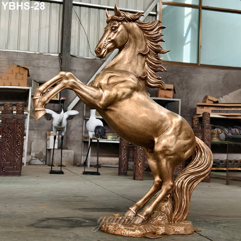 A gleaming bronze horse statue in a rearing pose, detailed muscular form, flowing mane, displayed inside a workshop or studio setting.