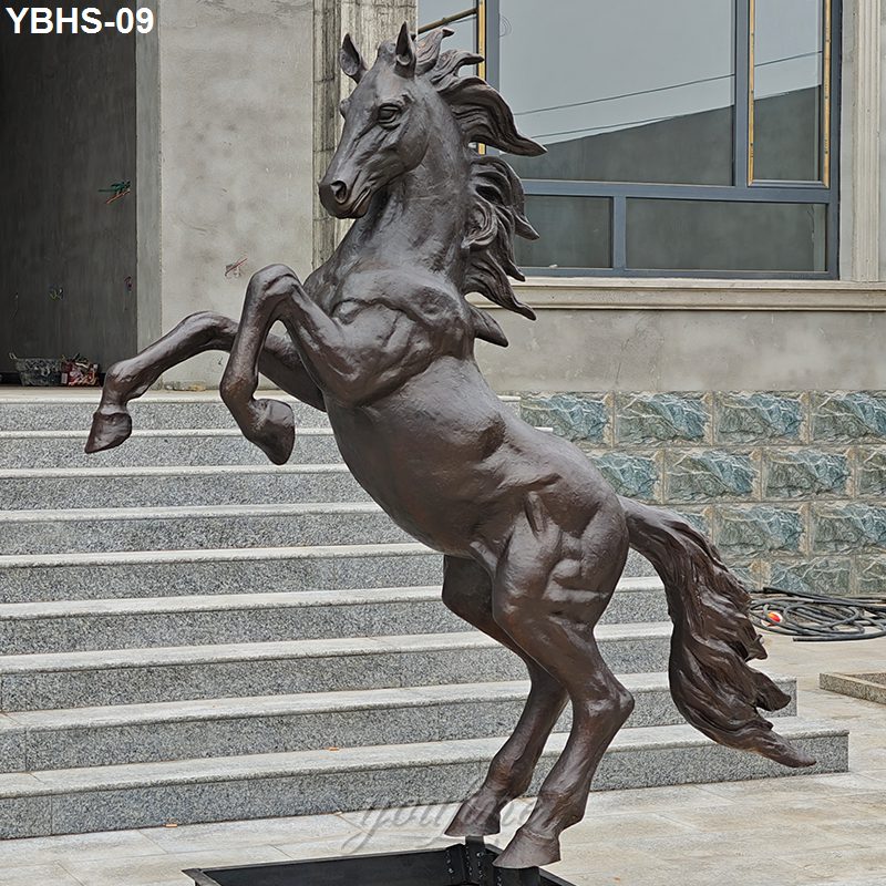 A dynamic bronze horse sculpture in a rearing pose with flowing mane, displayed on an outdoor staircase near a stone and glass structure.