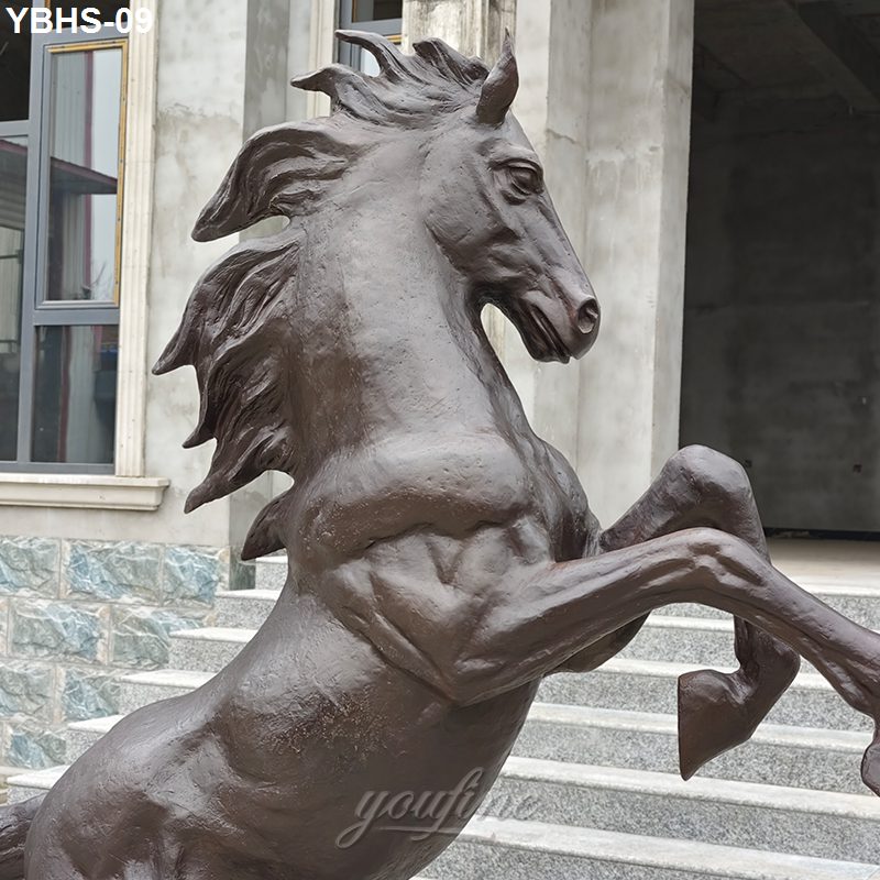 Bronze rearing horse statue featuring dynamic mane and muscular details, placed outdoors near stone steps and modern architecture.