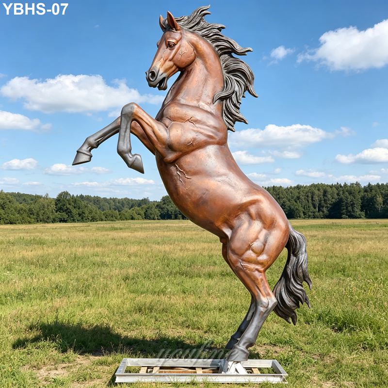 A dynamic bronze statue of a rearing horse with flowing mane, set in a lush open field under a sunny, blue sky.