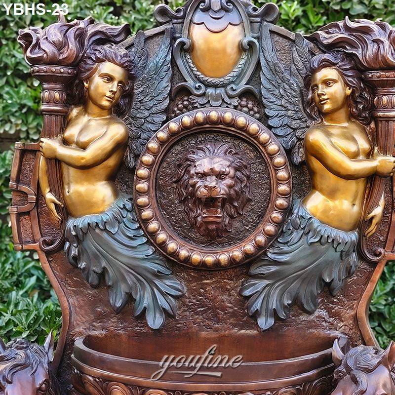 Intricate bronze wall fountain featuring a carved lion motif surrounded by winged mermaid figures holding torches, set against greenery.