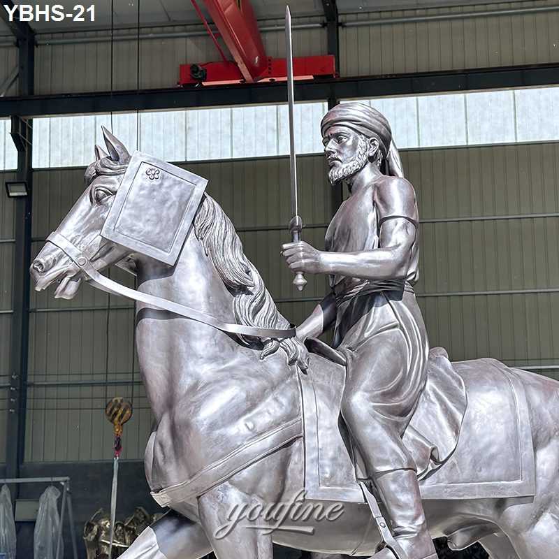 A detailed bronze sculpture of a warrior on horseback holding a sword, with ornate elements, displayed in an indoor workshop setting.