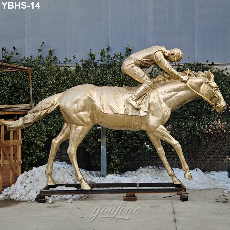 A golden bronze sculpture of a racehorse with a jockey in mid-race position, placed outdoors beside greenery.