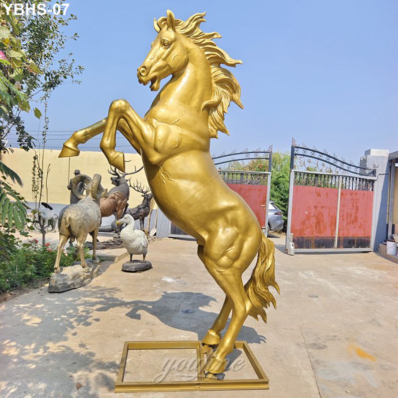 A golden bronze horse sculpture in a rearing pose displayed outdoors. Other animal statues and a gated area are visible in the background.