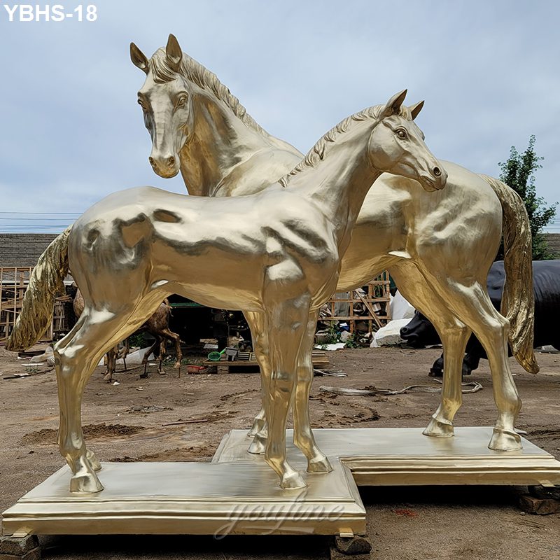 Two metallic golden bronze horse sculptures standing on square bases in an outdoor workshop setting, showcasing intricate detailing.